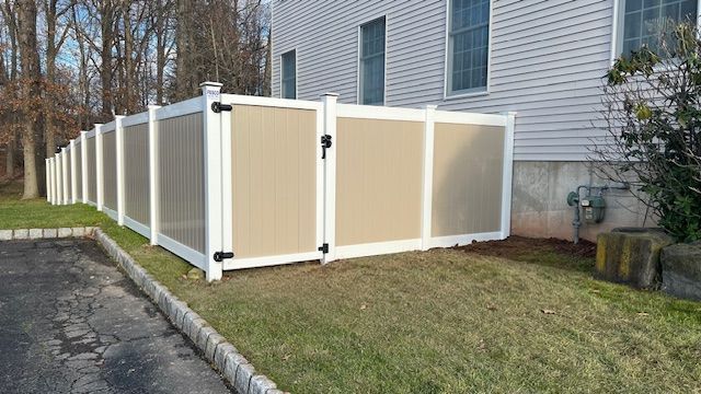 Tan and white vinyl fence around a grassy yard, beside a beige house.