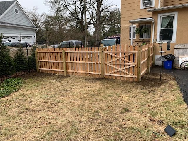Wooden picket fence enclosing a backyard with a gate, dry grass, and houses.