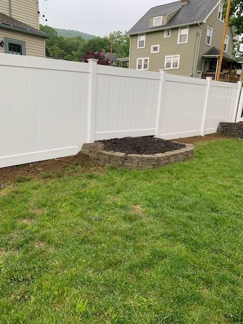 White vinyl fence in a grassy backyard, with a small brick garden bed.