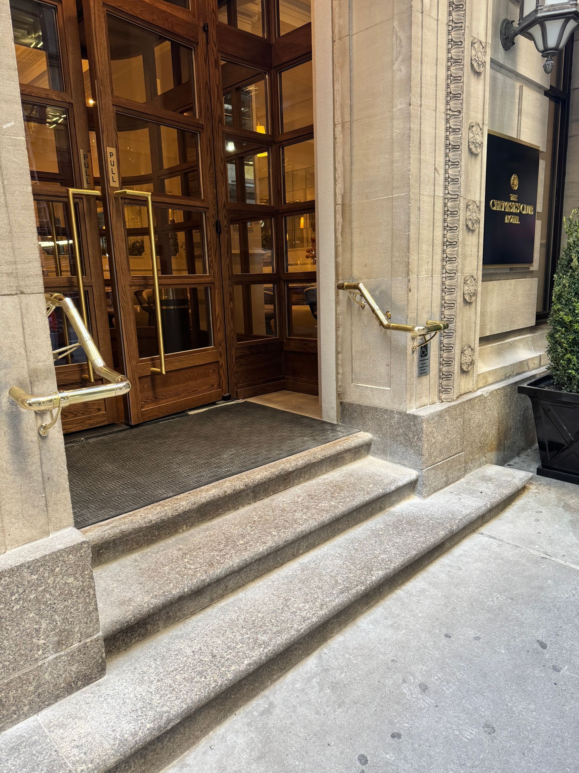 Stone entrance with steps and a ramp. Gold-trimmed glass doors lead into the building.