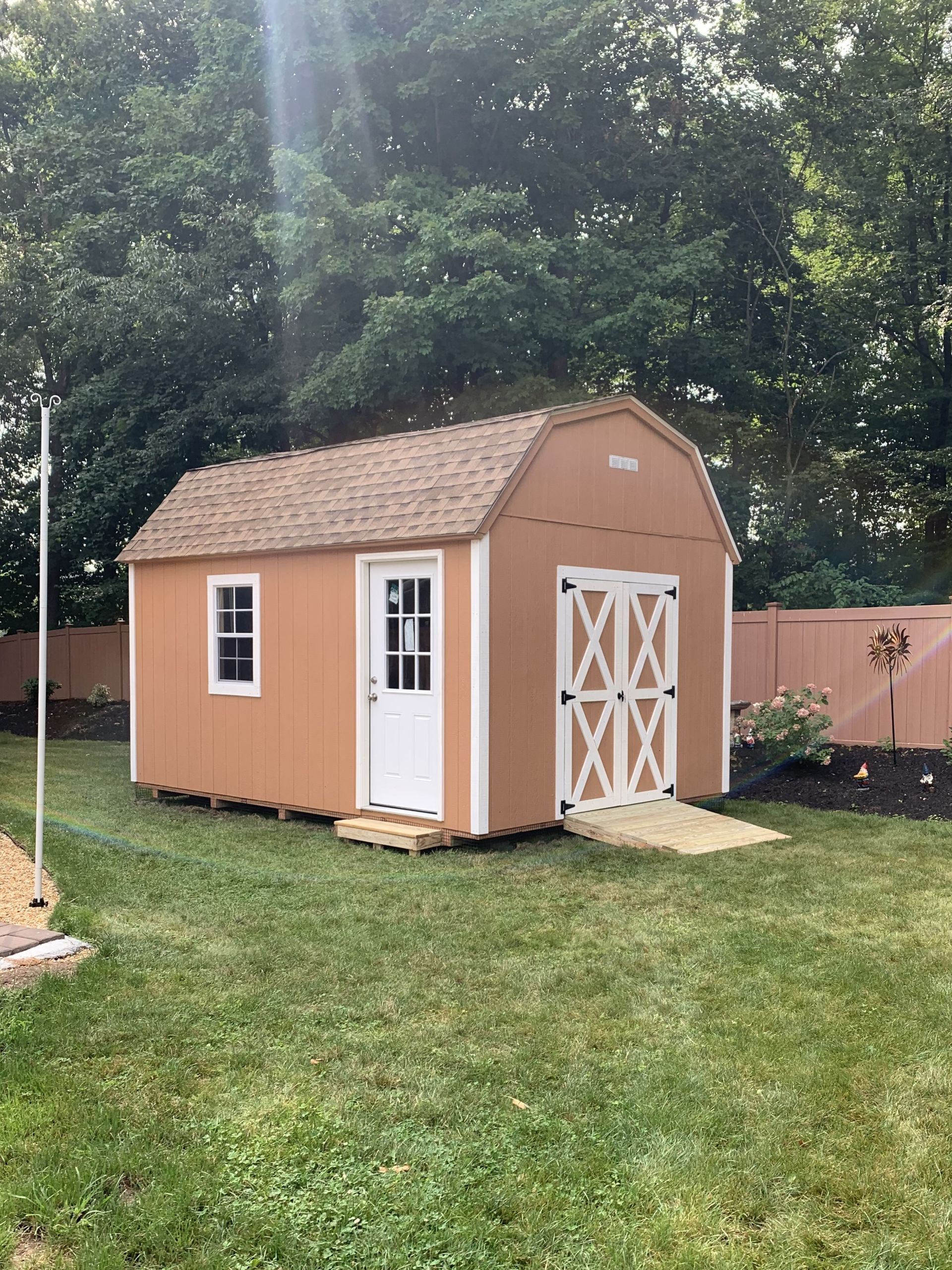 Tan barn-style shed in a grassy backyard with a ramp leading to the double doors.