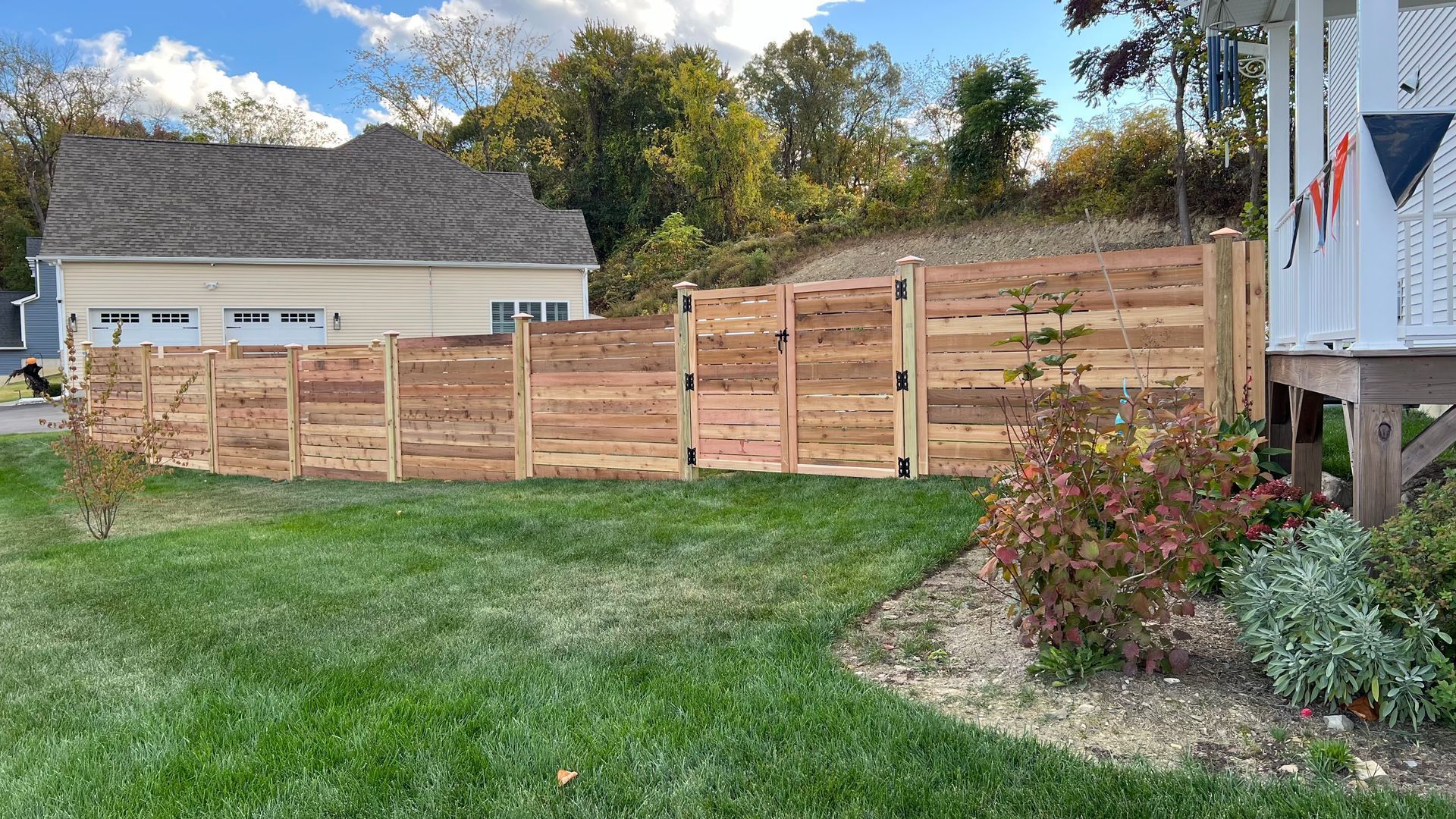 Wooden fence with two gates in a grassy backyard, adjacent to a house and a small deck.