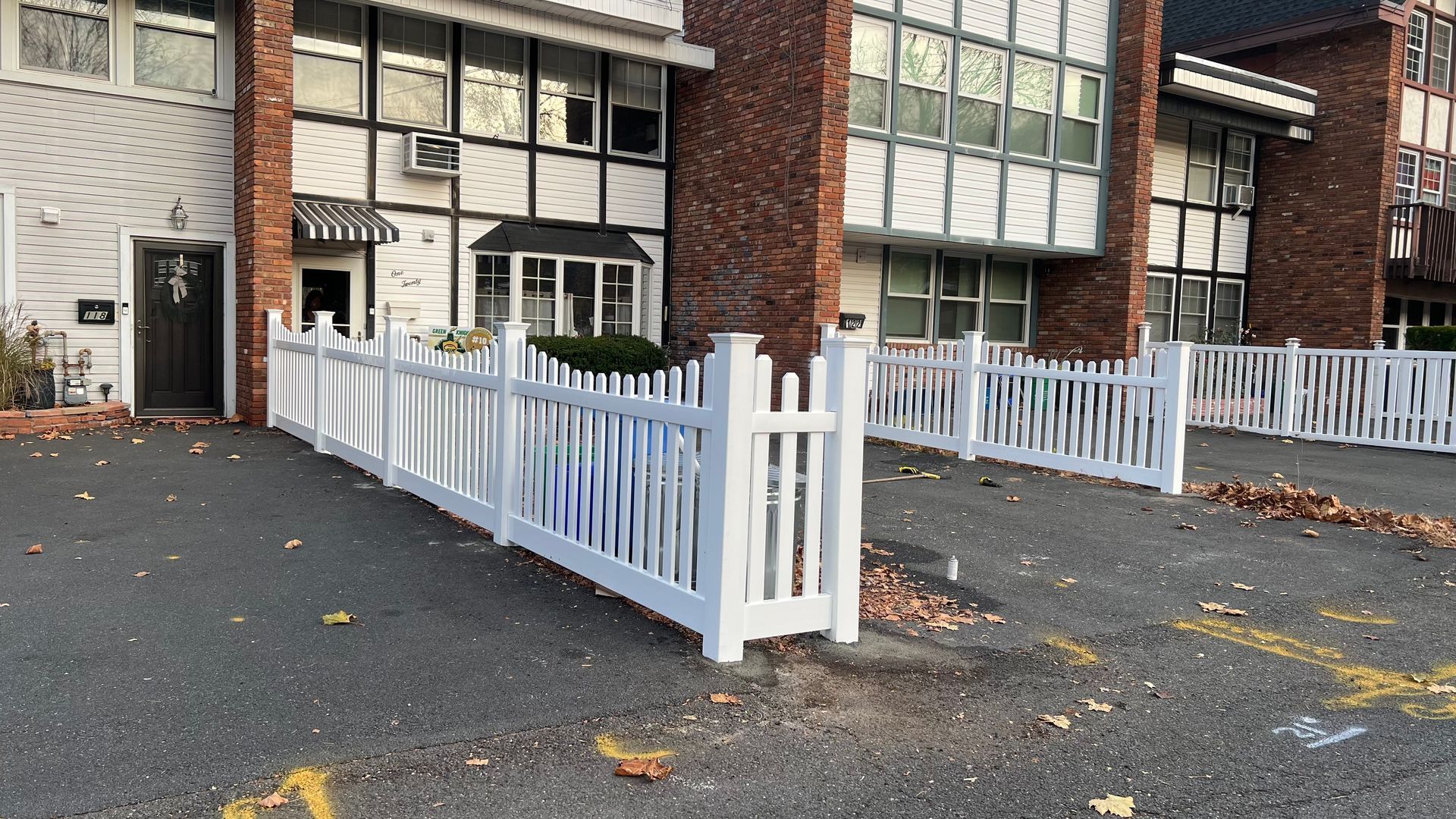 White picket fence in front of a brick building.
