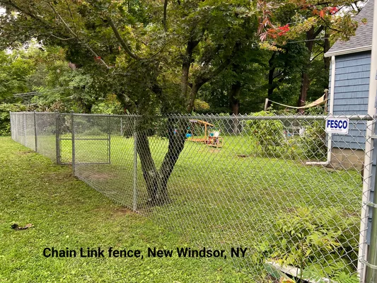 Chain-link fence in New Windsor, NY, surrounds a backyard with a tree and a small play structure.