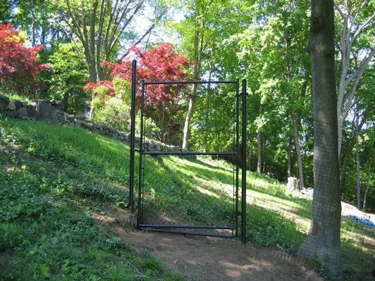 Black metal gate on a grassy hillside path, with trees in the background.