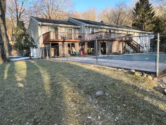 Two-story house with a wooden deck overlooking a fenced-in pool and grassy yard.