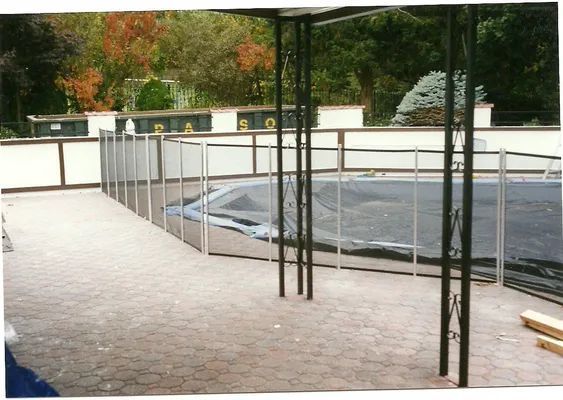 Patio with a pool covered by a tarp, surrounded by a fence and a black metal pergola.