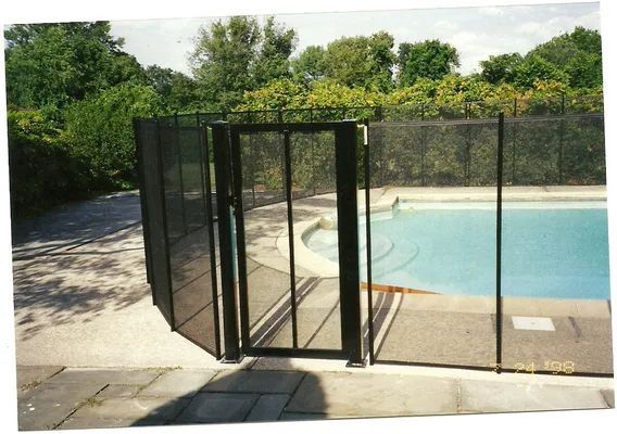 Black mesh pool fence with a gate, installed on a concrete patio, with a pool in the background.