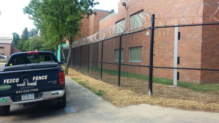 Black Fesco Fence truck parked next to a brick building with a fence topped with razor wire.