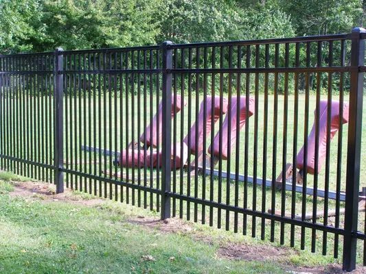 Black metal fence with vertical bars, enclosing red industrial equipment on green grass.
