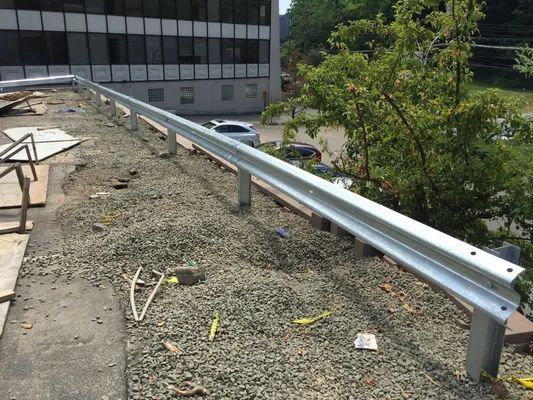 Metal guardrail on a gravel-covered rooftop, likely for safety. A building and trees are in the background.