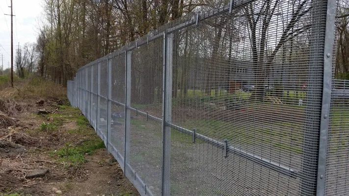 Metal mesh fence along a dirt path, trees in the background.