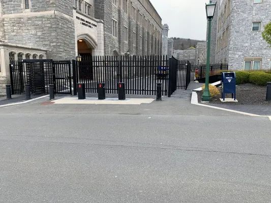 Metal security gates at building entrance, black bars, stone facade, asphalt road, green pole with light.