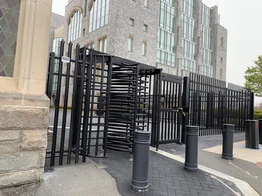 Black security turnstiles and fencing in front of a modern gray stone building.