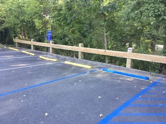 Parking lot with blue and yellow bumpers, wooden railing, trees in background.