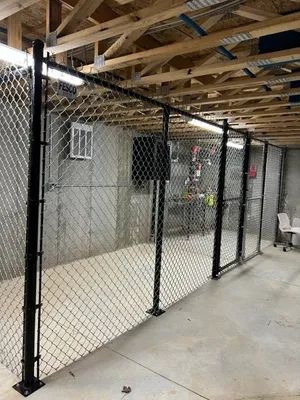 Black chain-link fence installed inside a room with concrete walls and wooden beams on the ceiling.