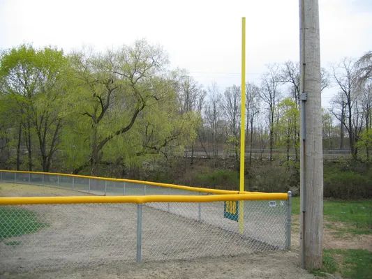 Baseball field with yellow foul pole and fence, trees in background.