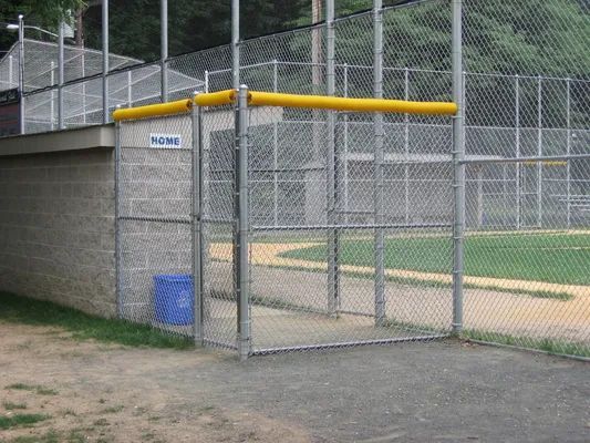 Entrance to a baseball dugout, gray concrete, chain-link fence, yellow padding, blue trash can.