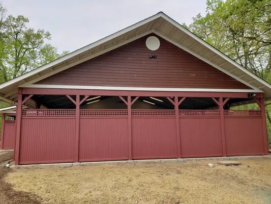 Red picnic shelter with wood siding, in a park.