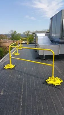 Yellow safety railings on a flat rooftop. Bright blue sky overhead.