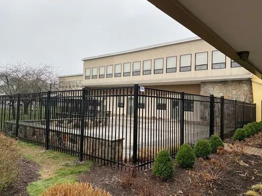 Black metal fence surrounding a building with multiple windows. Overcast sky.