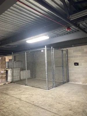 Metal chain-link storage cage in a warehouse with a concrete floor and overhead lighting.