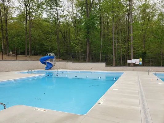 Outdoor swimming pool with a blue slide, surrounded by trees.