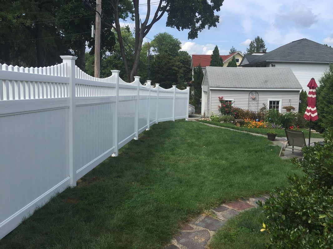 White vinyl fence borders a green lawn in a yard, leading to a small building.