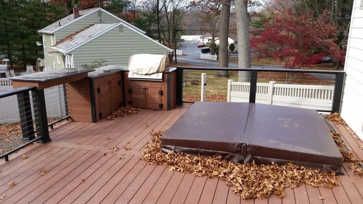 A deck with a brown hot tub covered in leaves and a built-in outdoor kitchen.