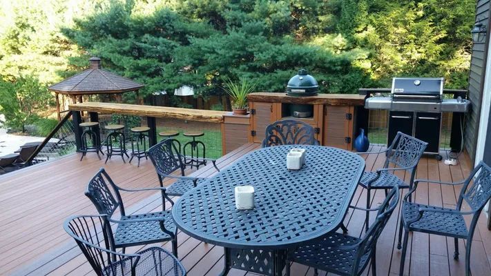 Outdoor deck with grill, bar, and table seating; brown composite decking and green foliage background.