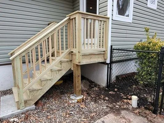 Wooden outdoor staircase leading to a small deck with railings, attached to a house with gray siding.
