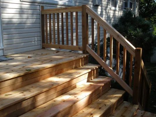 Wooden deck and staircase with a railing leading to a house.