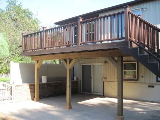Brown deck with stairs, supported by wooden posts, over a concrete patio.