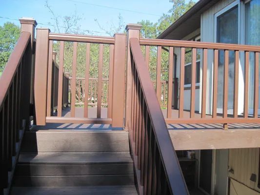 Brown wooden deck with stairs and railing. A gate is visible. Sunlight shines on the structure.