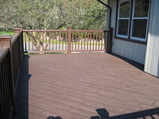 Brown wooden deck with railings, next to a beige house, sunny outdoor setting.