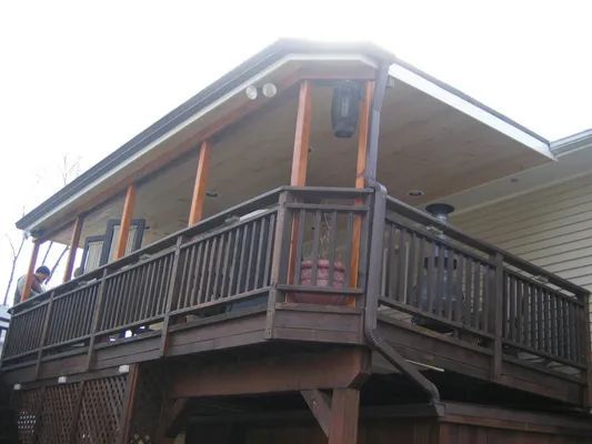 Brown wooden deck with screened-in porch, attached to a house with beige siding. Overcast sky.