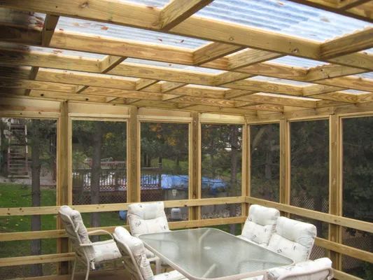 Wooden screened-in porch with translucent roof and outdoor furniture; trees and lawn visible in the background.