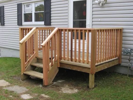 Wooden deck with stairs leading to a back door of a home with gray siding and shuttered window.