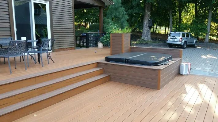 Wooden deck with a hot tub, steps, and outdoor furniture. A vehicle is parked in the driveway.