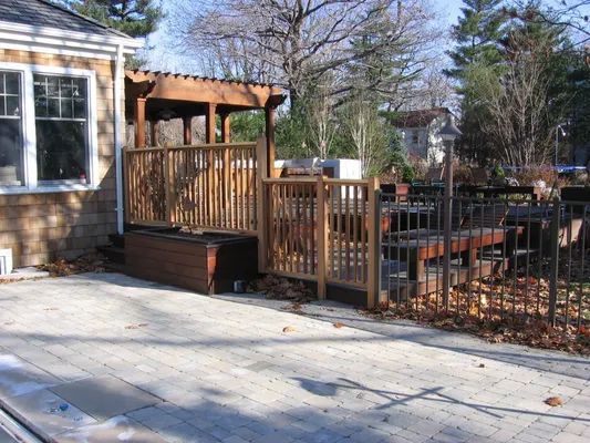 Wooden deck with a pergola, next to a house with a concrete patio.