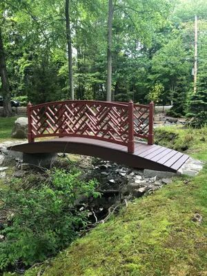 Red wooden bridge over a creek in a park with lush greenery.