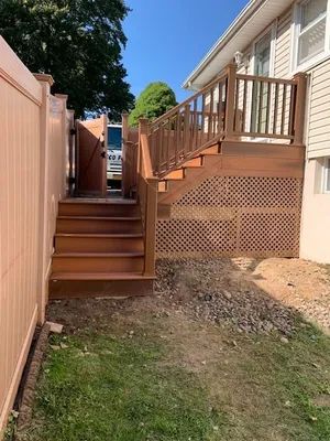 Wooden deck with stairs, lattice detail, adjacent to house and tan fence, on grassy area.