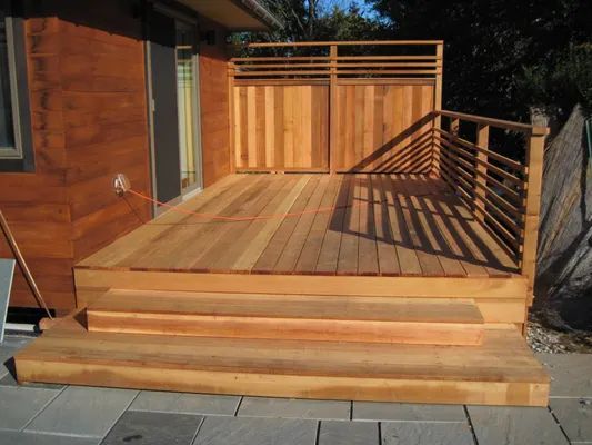 Wooden deck with steps, railings, and privacy screen against a building.