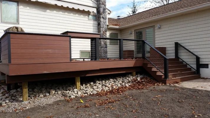 Brown composite deck with black railing and steps attached to a white house.