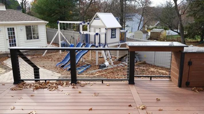 Deck with a playground in the background. Brown decking and railing, swings, slide and playhouse. Fallen leaves.