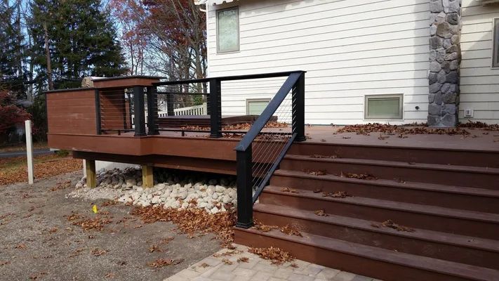Brown wooden deck with black railing and steps attached to a white house.
