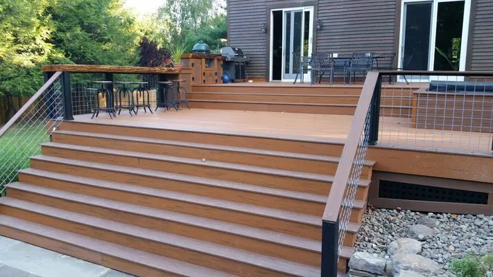 Brown wooden deck with stairs and cable railing; outdoor setting.