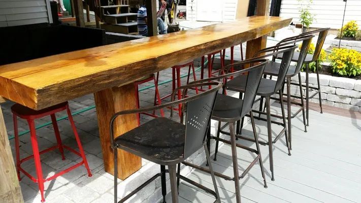 Outdoor bar with long wooden countertop and metal stools.