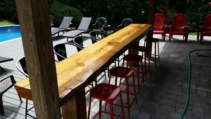 Outdoor bar with wooden countertop and red stools, next to a pool.