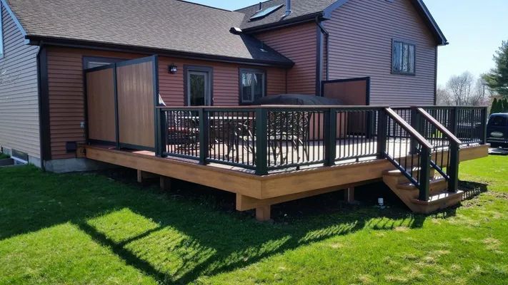 Wooden deck with black railings and privacy panels on a house with brown siding.